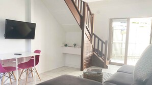 A living room with a grey sofa, a small table with a TV, and a staircase. - Byron Springs (Byron Bay)