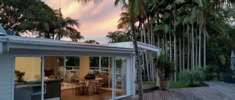 A modern house with a covered patio, a dining area, and a kitchen visible through glass doors.