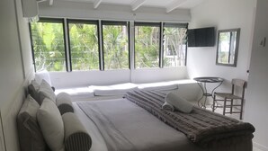 A bedroom with a large bed, a small table, a chair, and a TV on the wall. - Byron Springs (Byron Bay)