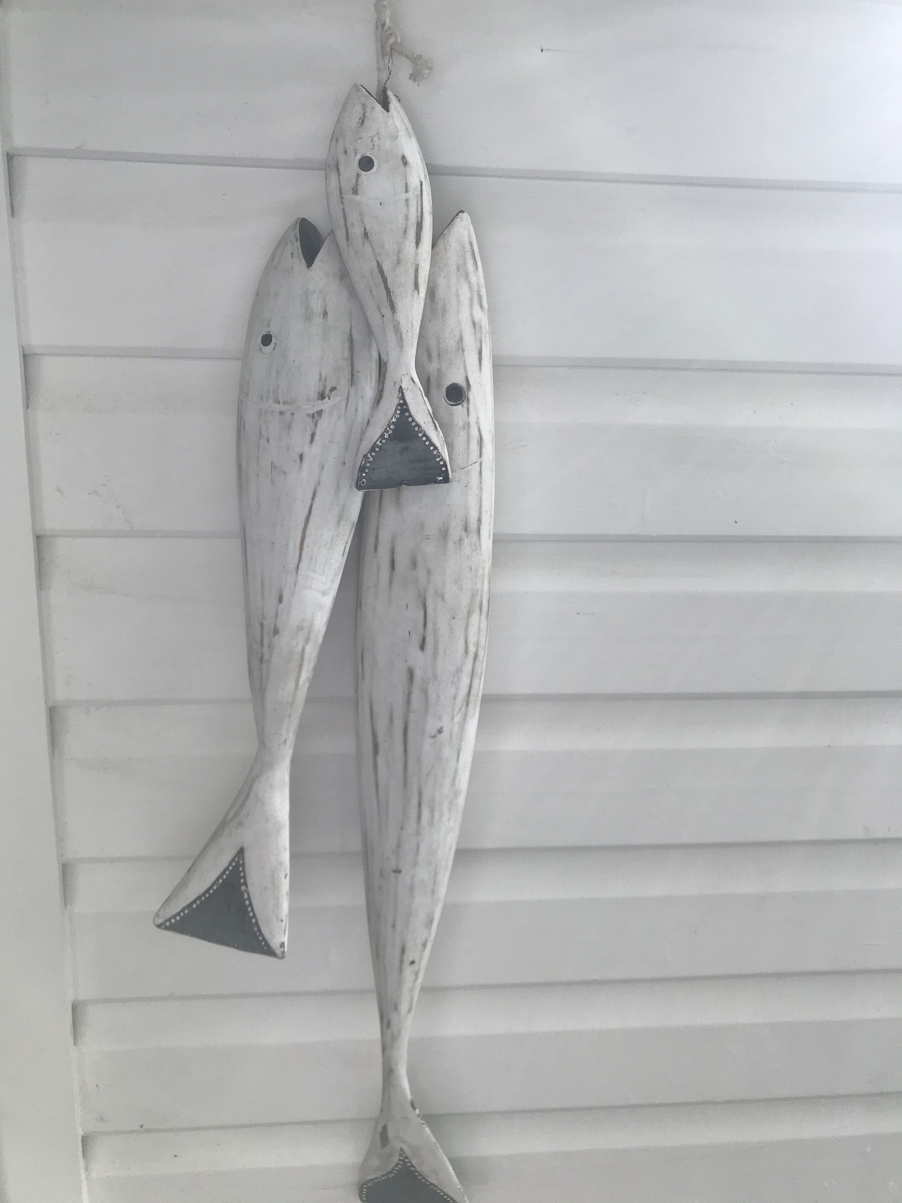 Dos adornos con forma de pez colgados en una pared blanca con líneas horizontales.