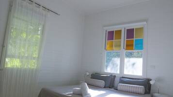A bedroom with a bed, a ceiling fan, a window with colorful panes, and a bedside lamp.