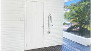 A white door with a number "5" on it, a small window with a view of palm trees and a building, and a wooden deck. - Byron Springs (Byron Bay)