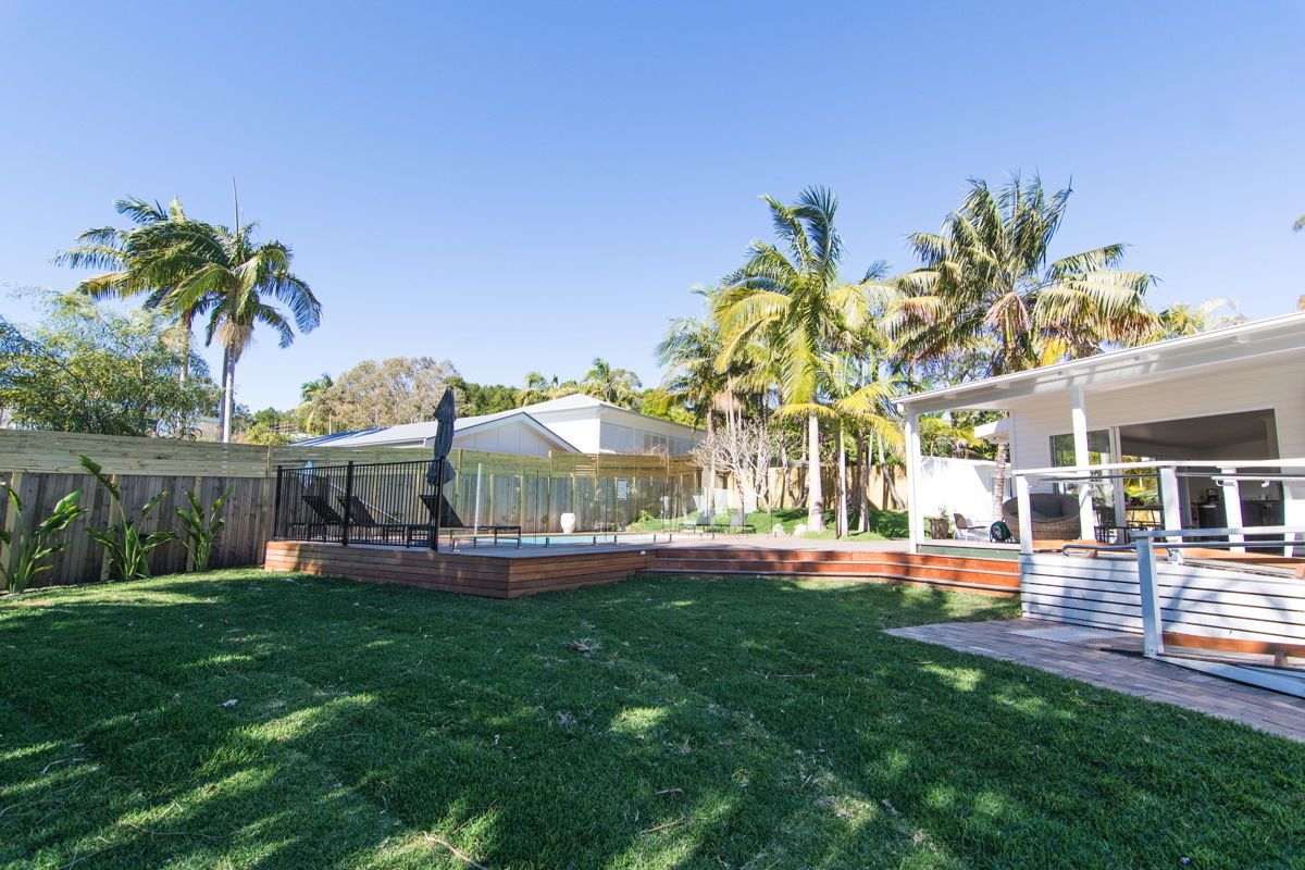 A modern house with a covered patio, a fenced backyard, and palm trees.