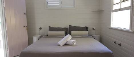 A bedroom with a bed, two bedside tables, a window, and a door.