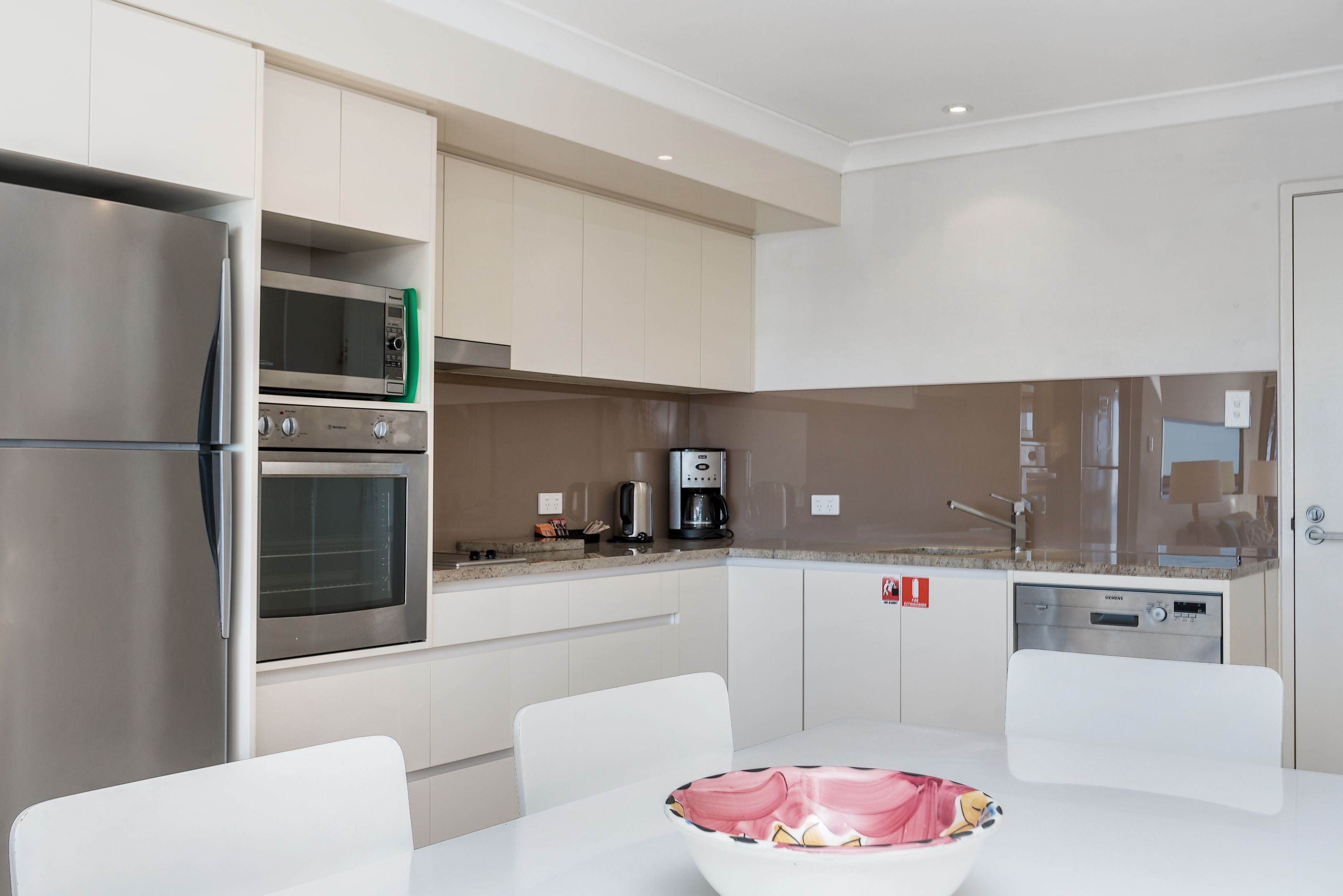 Une cuisine moderne dotée d’appareils électroménagers en acier inoxydable, de meubles blancs et d’un coin repas avec une table et des chaises blanches.