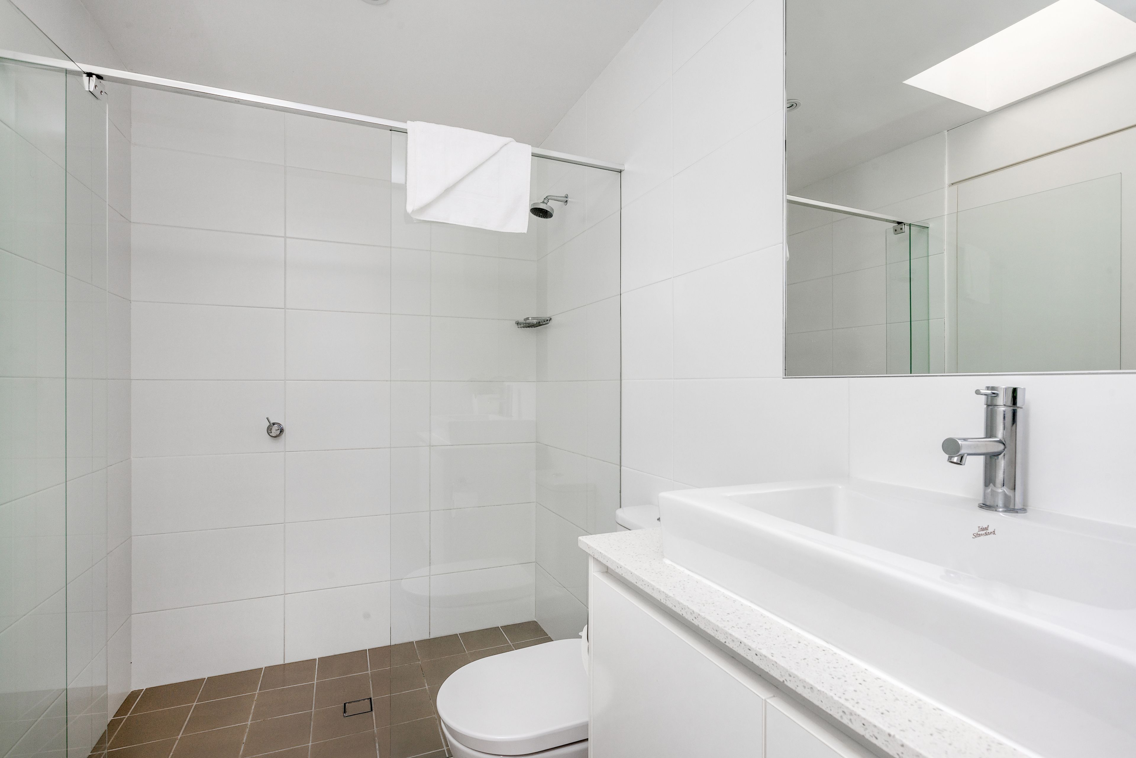 A modern bathroom with a glass shower enclosure, a white toilet, and a large mirror above the sink.