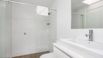 A modern bathroom with a glass shower enclosure, a white toilet, and a large mirror above the sink.