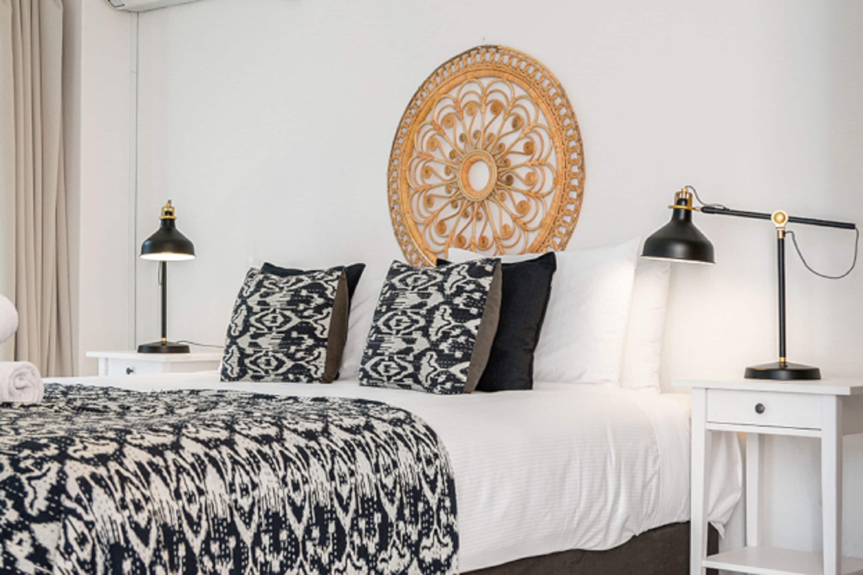A neatly arranged bedroom with a bed, two bedside tables, a wall decoration, and two lamps.