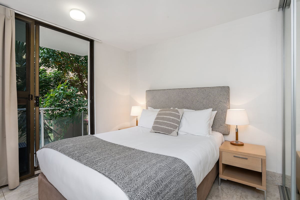 Ein Schlafzimmer mit Bett, Nachttischen, einer Lampe und einer Schiebetür zu einem Balkon.