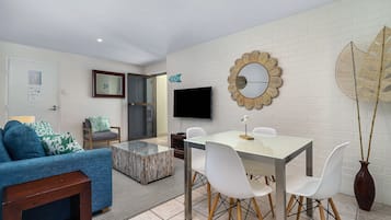 A modern living room with a sofa, coffee table, TV, and a dining area with chairs and a table.