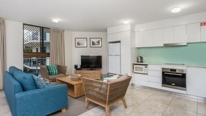 Una sala de estar moderna con un sofá, una silla de mimbre, un televisor y una zona de cocina con microondas y horno.