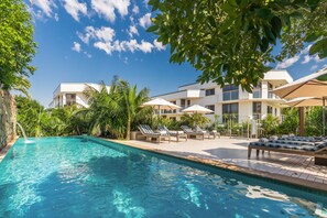 A swimming pool with lounge chairs and umbrellas, surrounded by lush greenery and modern buildings. - Bayview Beachfront Apartments, in town right on the beach (Byron Bay)