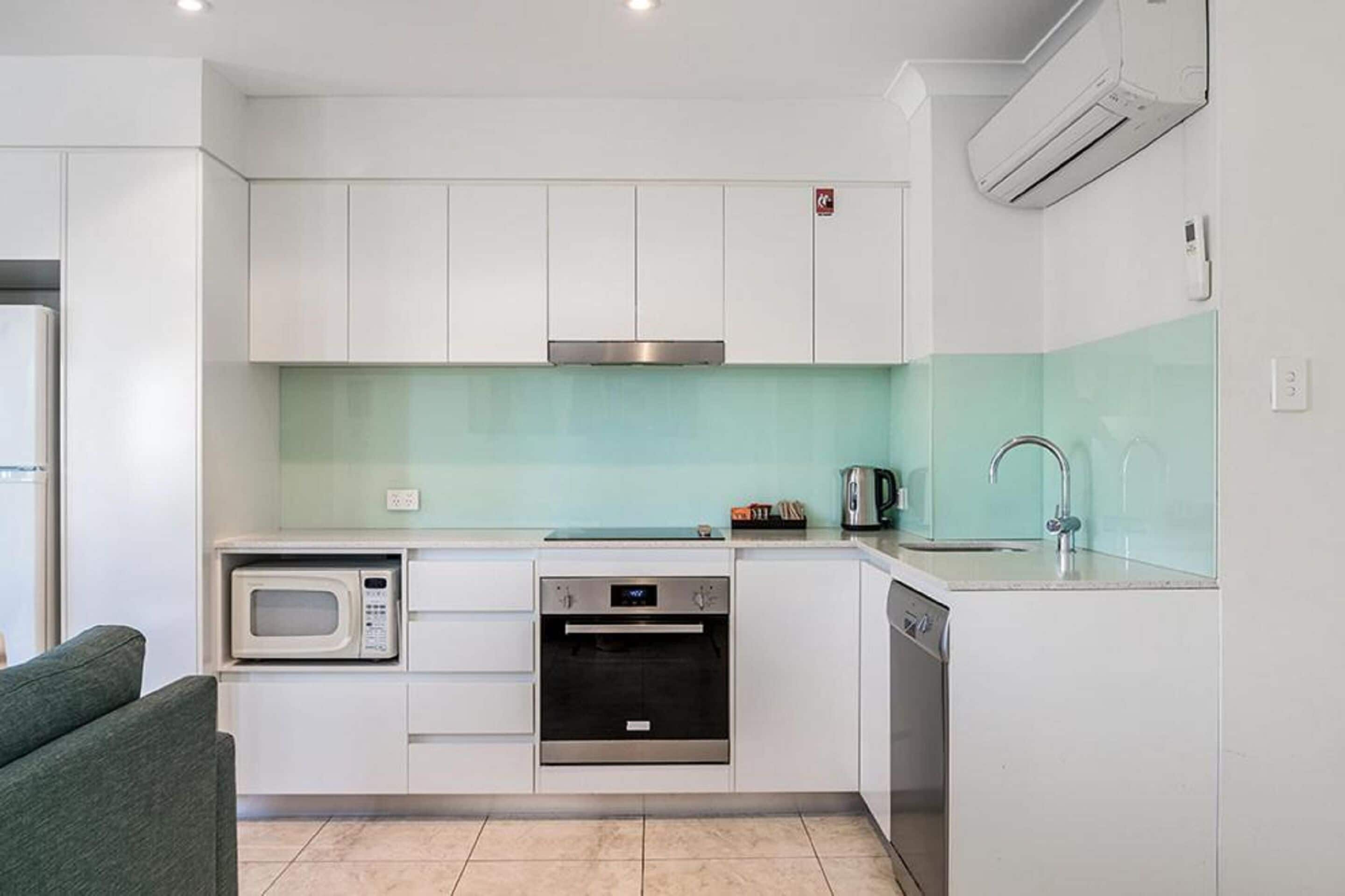 A modern kitchen with white cabinets, a stainless steel range hood, a microwave, an oven, a dishwasher, and a sink with a faucet.