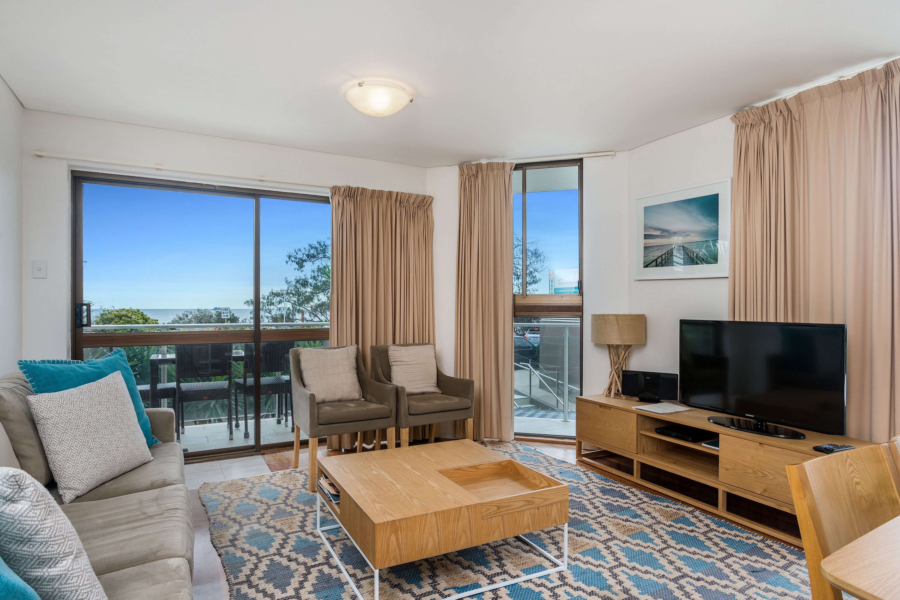 A modern living room with a sofa, two armchairs, a coffee table, a TV, and a balcony with a view.