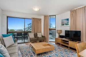 Una sala de estar moderna con sofá, dos sillones, una mesa de centro, televisor y un balcón con vistas.