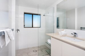A modern bathroom with a glass shower enclosure, a large mirror, and a sink with a towel rack. - Bayview Beachfront Apartments, in town right on the beach (Byron Bay)