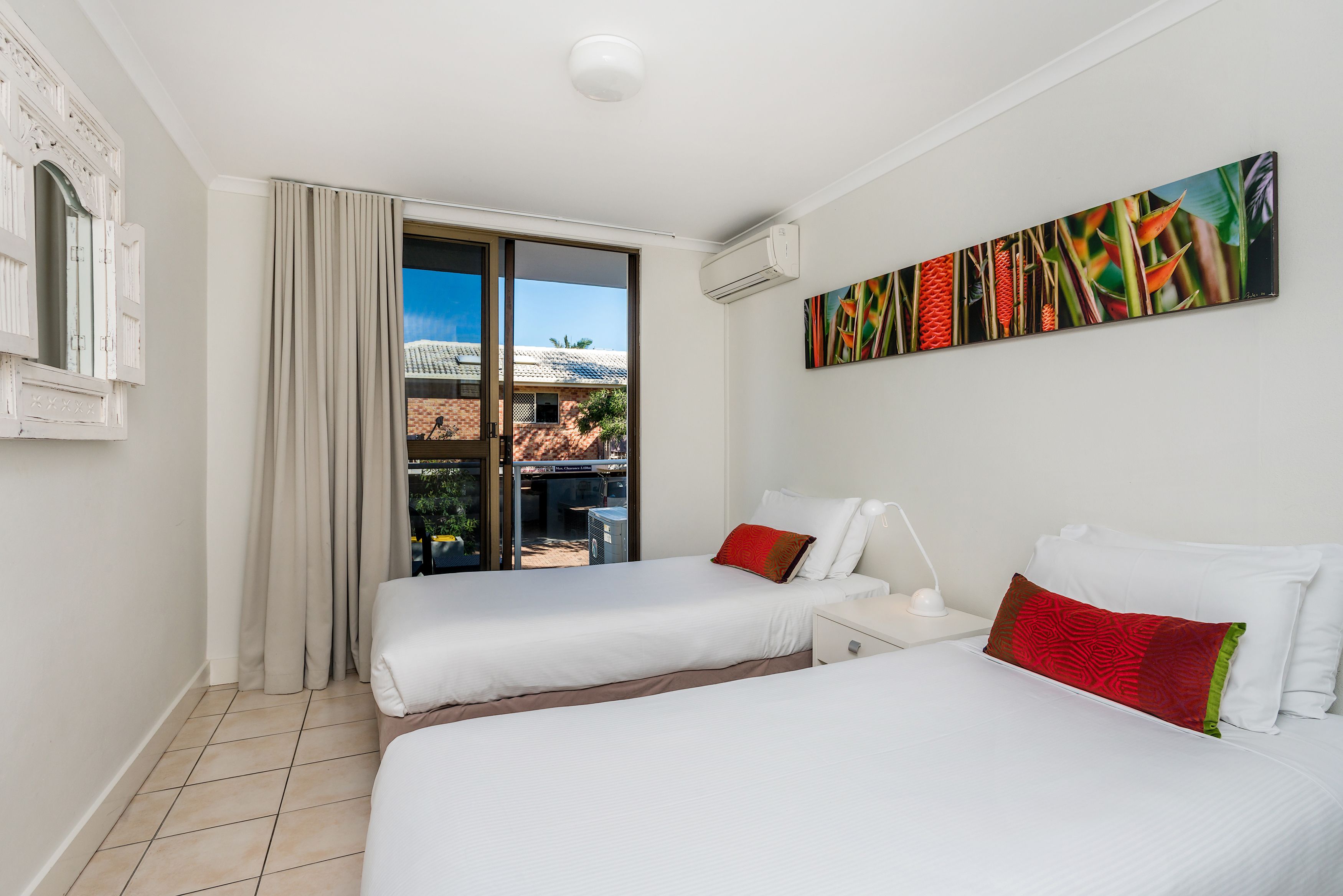 Una habitación de hotel con dos camas, un ventanal con cortinas, un ventilador de techo y un aire acondicionado instalado en la pared.