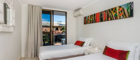 Una habitación de hotel con dos camas, un ventanal con cortinas, un ventilador de techo y un aire acondicionado instalado en la pared.