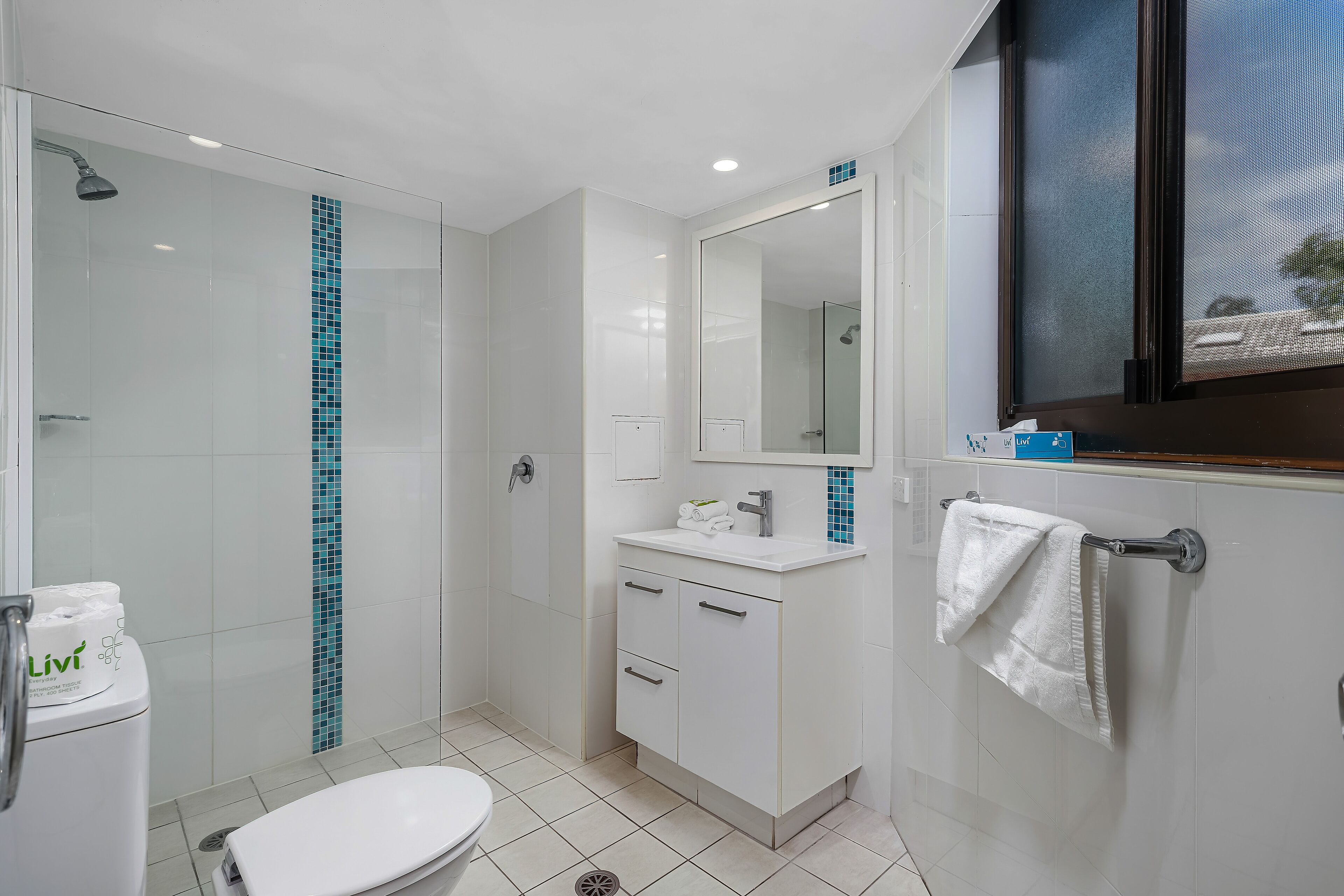 Un baño moderno con cabina de ducha de vidrio, tocador blanco y un espejo grande.