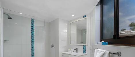 Un baño moderno con cabina de ducha de vidrio, tocador blanco y un espejo grande.