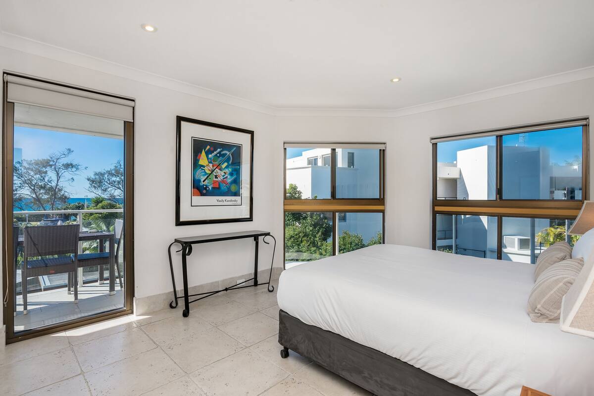 Ein modernes Schlafzimmer mit einem großen Bett, einem Schreibtisch und einem Balkon mit Stadtblick.