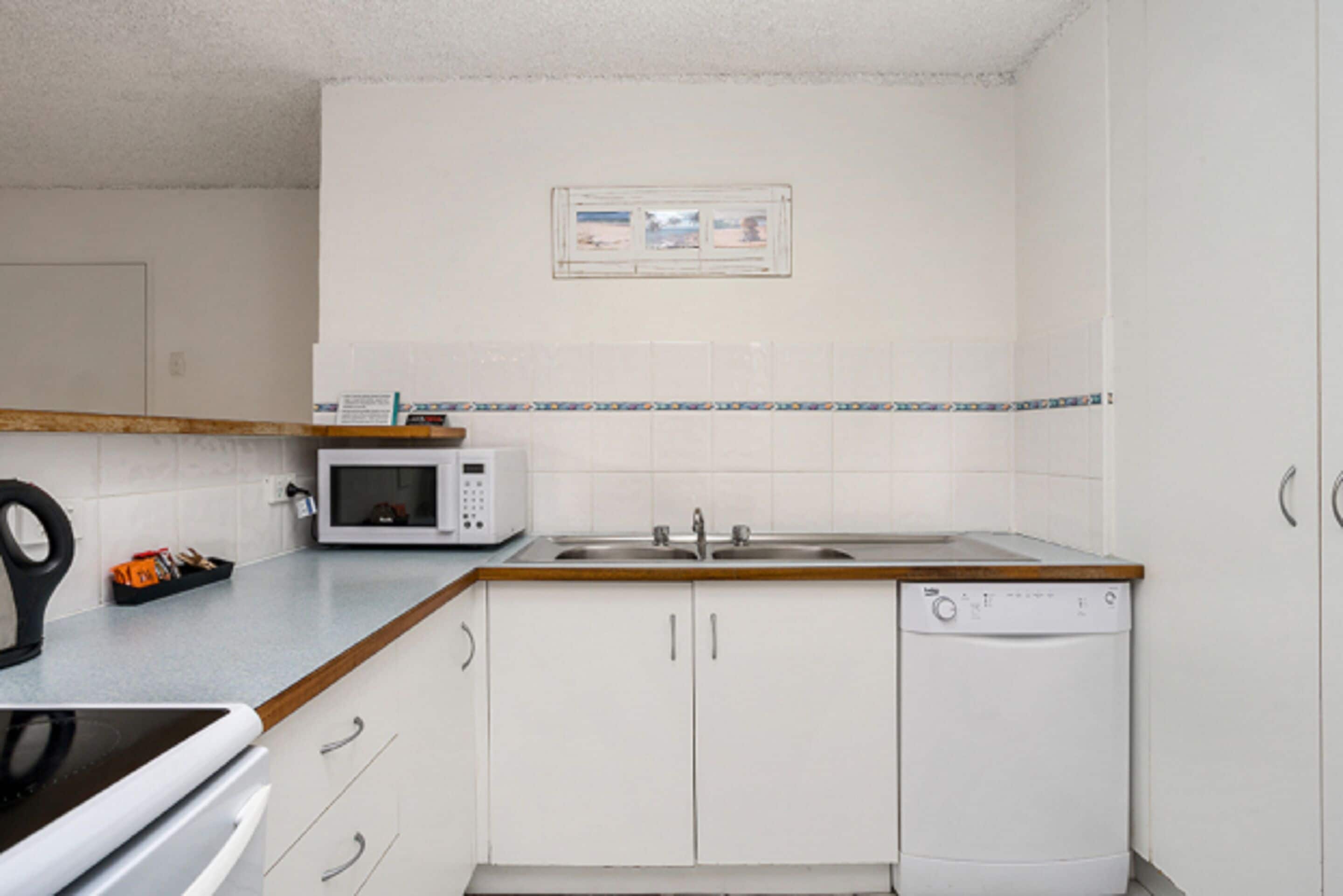 Una cocina compacta con armarios blancos, microondas, fregadero y lavavajillas.