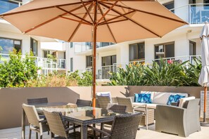 An outdoor patio with wicker furniture, a glass table, and a large umbrella. - Bayview Beachfront Apartments, in town right on the beach (Byron Bay)