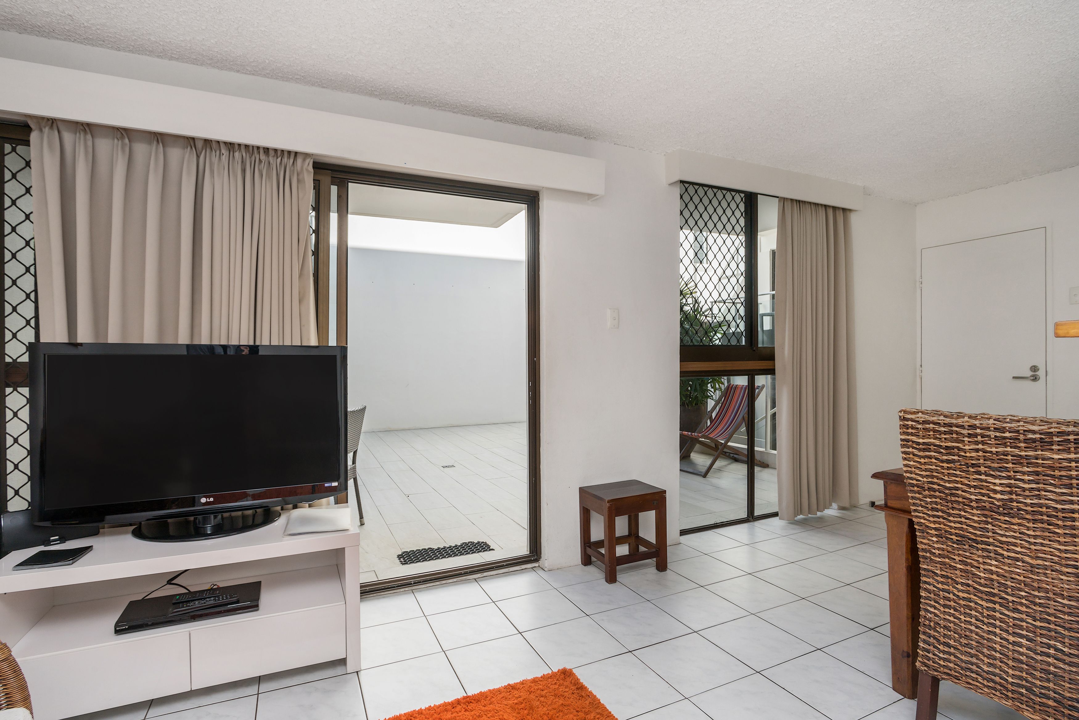 Una sala moderna con un televisor de pantalla plana, un taburete de madera y un sillón de mimbre.
