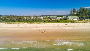 Una playa con gente, un edificio de techo verde y árboles al fondo.