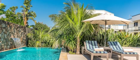 Una piscina al aire libre, sombrillas, sillones reclinables de piscina