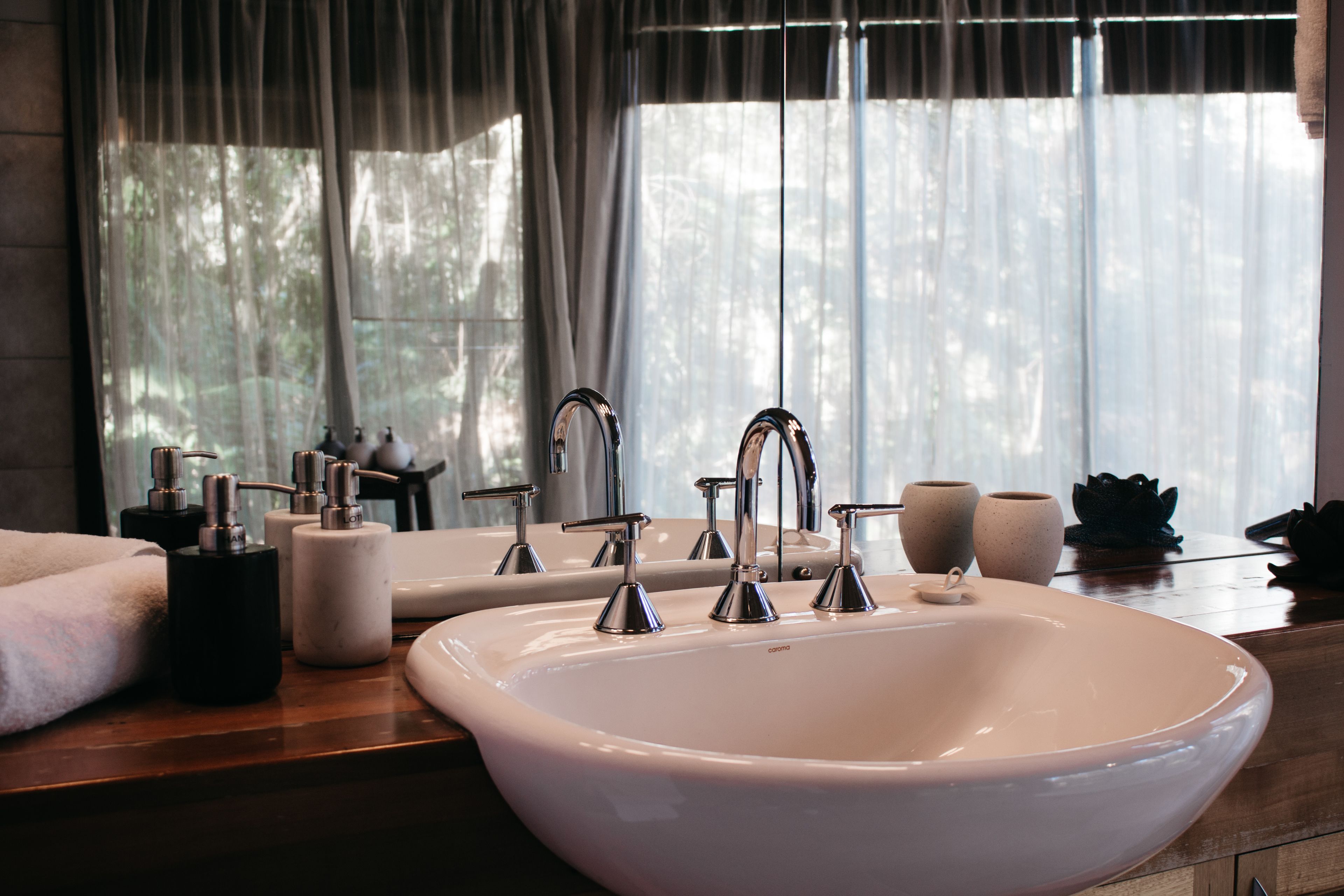 A bathroom with a large white sink, two faucets, and a mirror. There are two ceramic cups and a black soap dispenser on the counter.