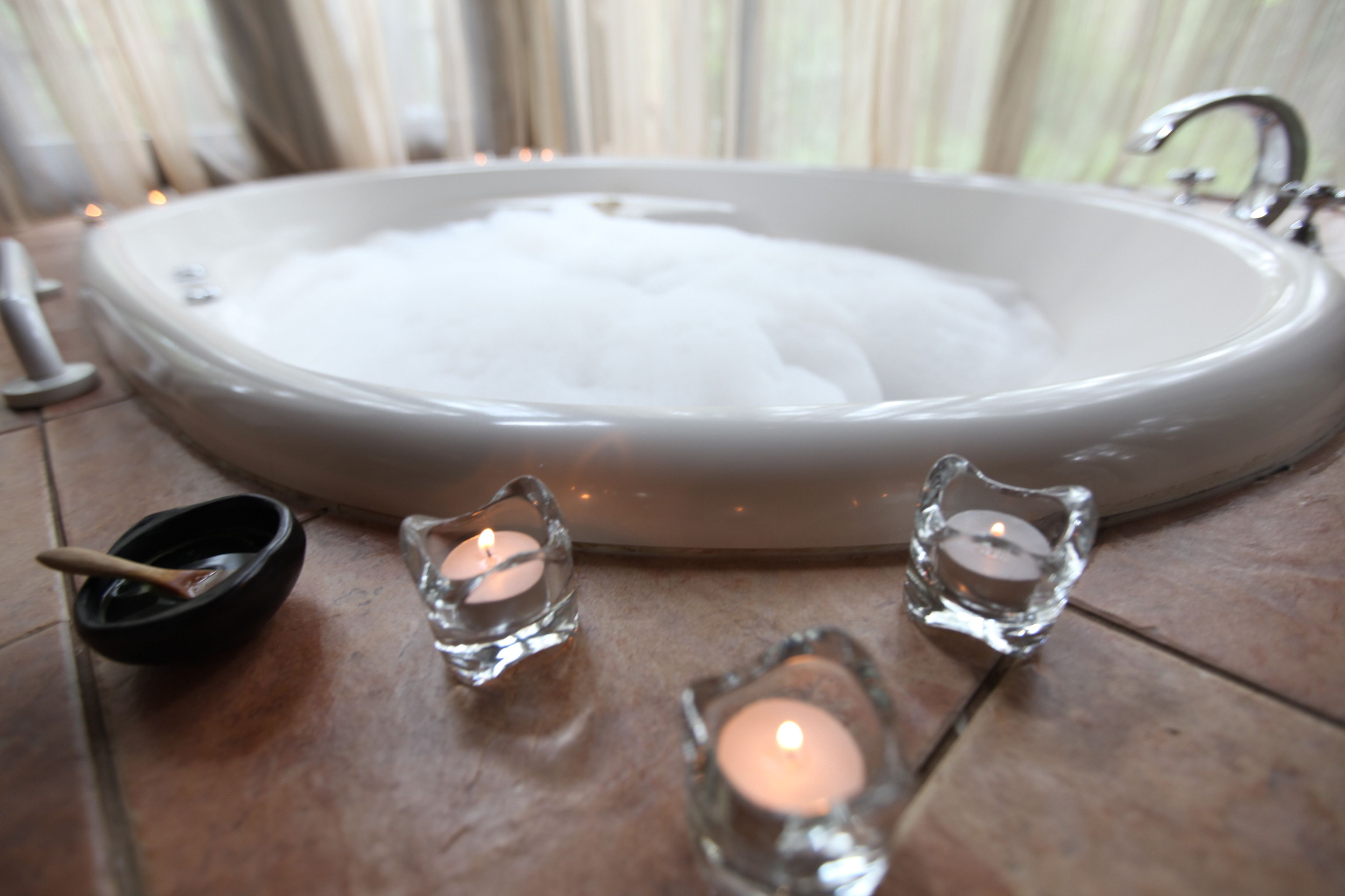 A bathroom with a large bathtub filled with bubbles, a sink, and two glass candle holders with candles.