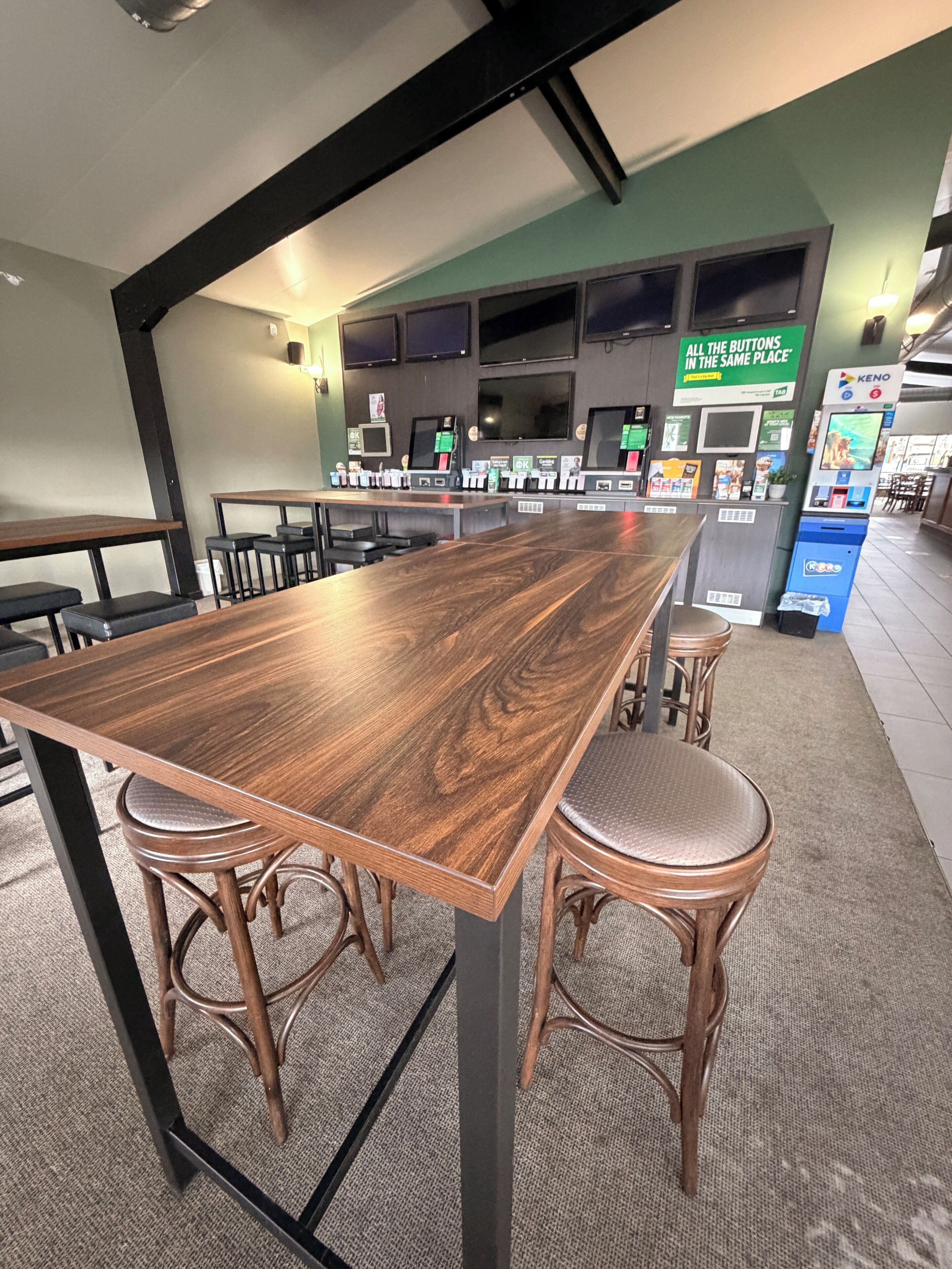 A long wooden table with four stools, a KENO machine, and a green sign with text.