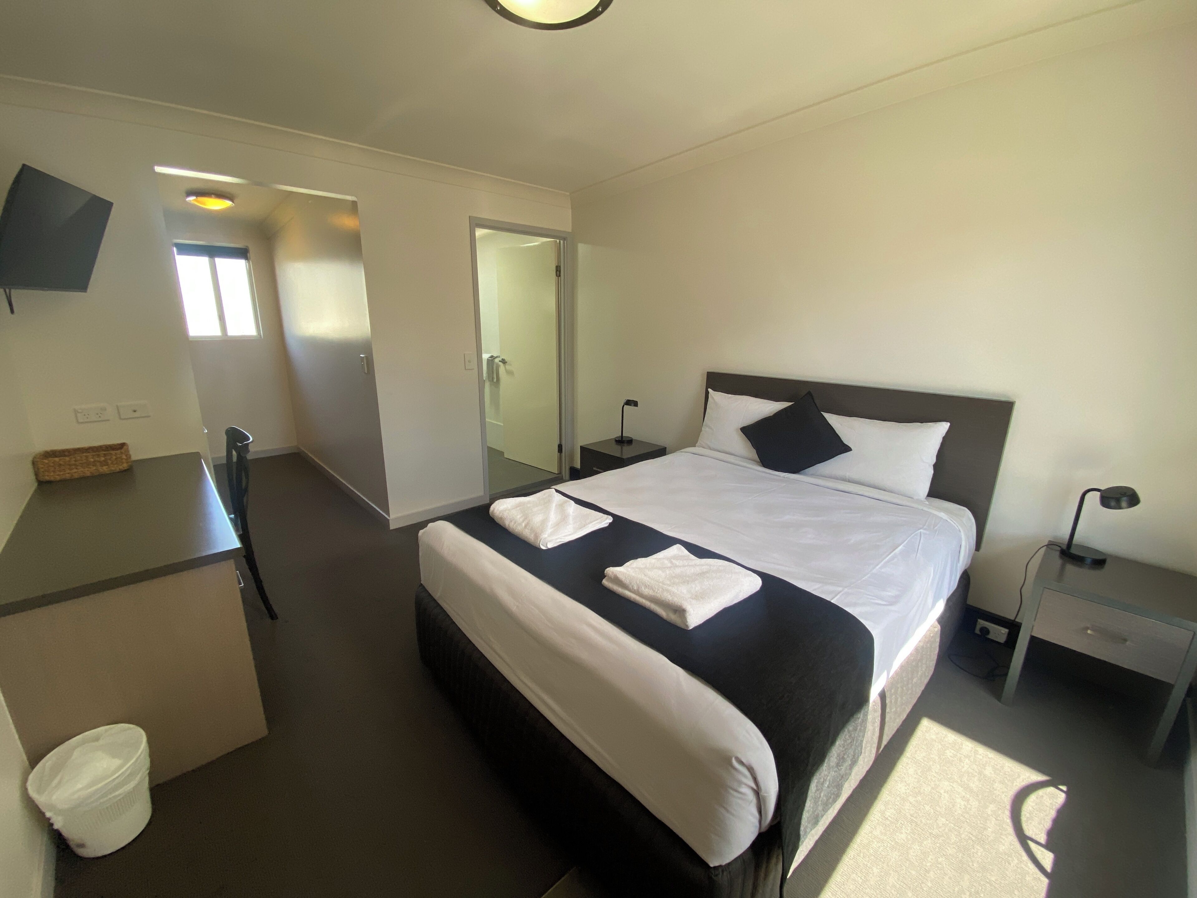 A hotel room with a bed, bedside tables, a desk, and a chair.
