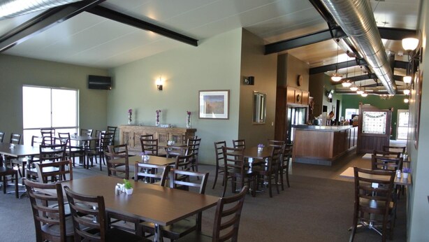 A spacious dining area with multiple tables and chairs, a bar counter, and a large window providing natural light.