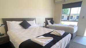 Two double beds with black and white bedding, a bedside table with a lamp, and an air conditioning unit on the wall.
