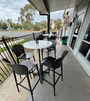 An outdoor patio area with a round table and chairs, a trash bin, and a building with a sign. - Dooleys Springsure Tavern and Motel (Springsure)