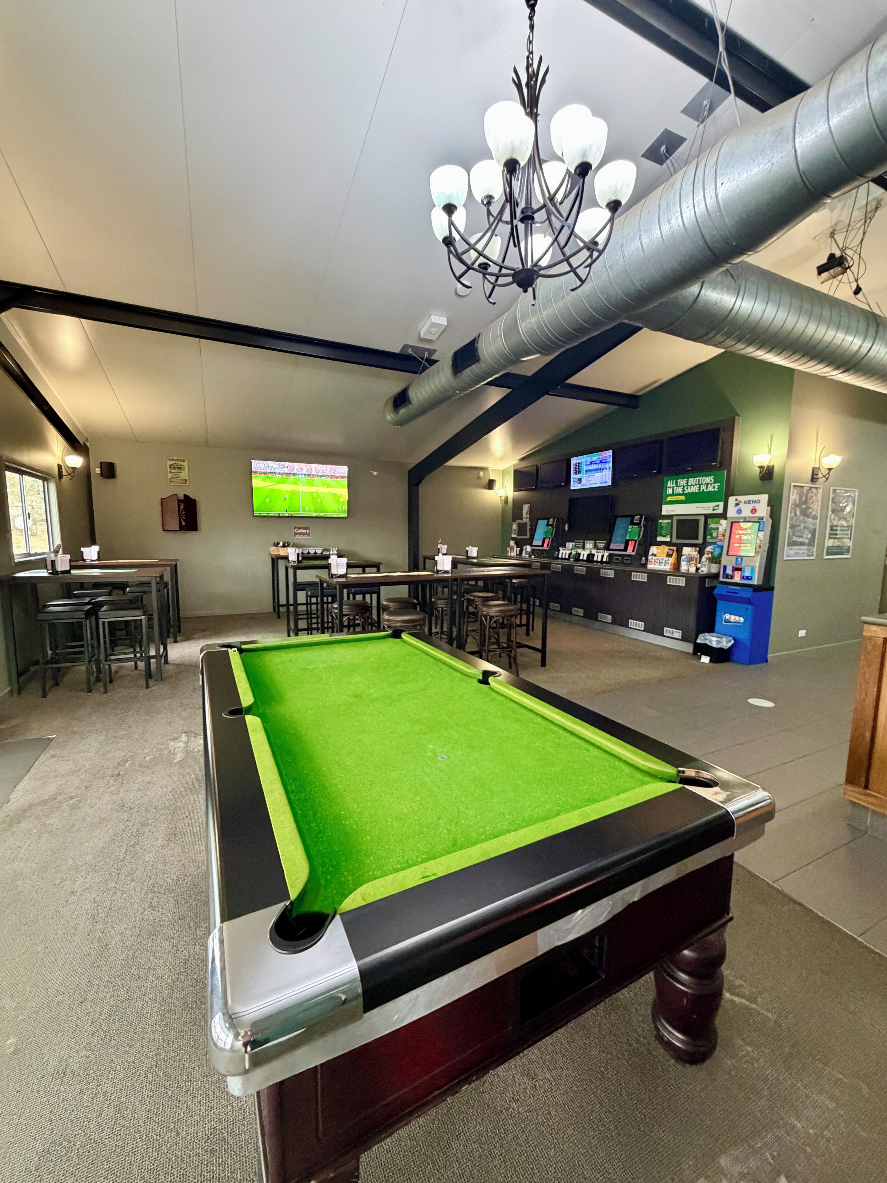 A pool table with a green felt surface, a bar area with stools, and a television screen displaying a sports event.
