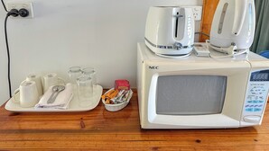 A microwave oven with a digital display, a kettle, and a tray with cups and a spoon. - Ocean View Motel Bowen (Bowen)