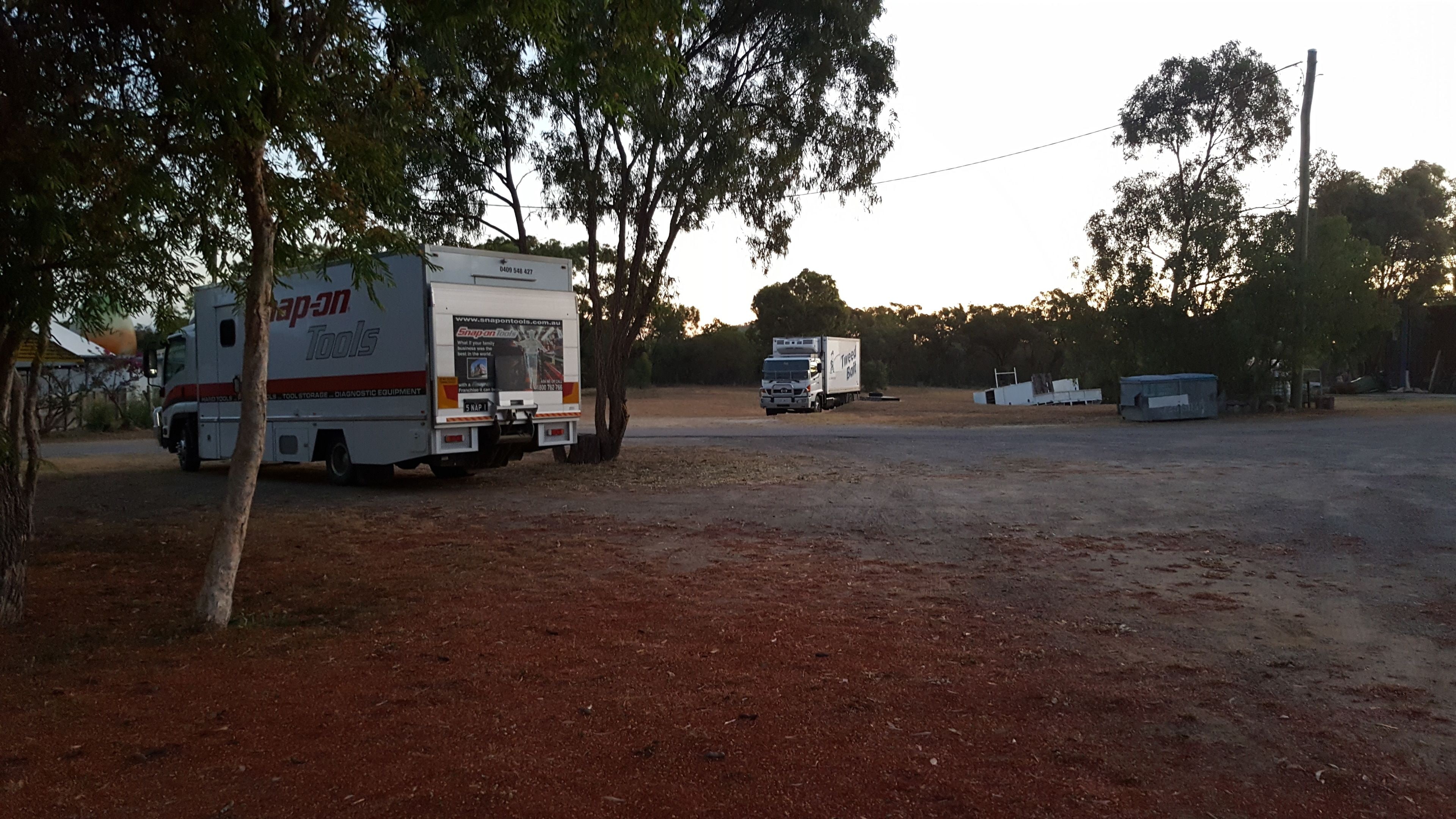 A truck with 'Snap-on Tools' branding parked in a rural area with trees and a dirt ground.