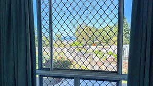 A room with a large window featuring a metal grid, curtains, and a view of a parking area and greenery outside. - Ocean View Motel Bowen (Bowen)