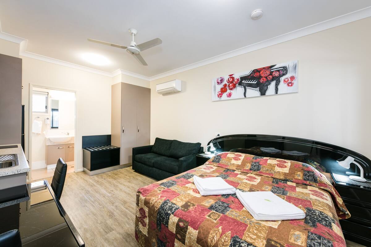 A hotel room with a bed, a desk, a chair, a sofa, and a ceiling fan.