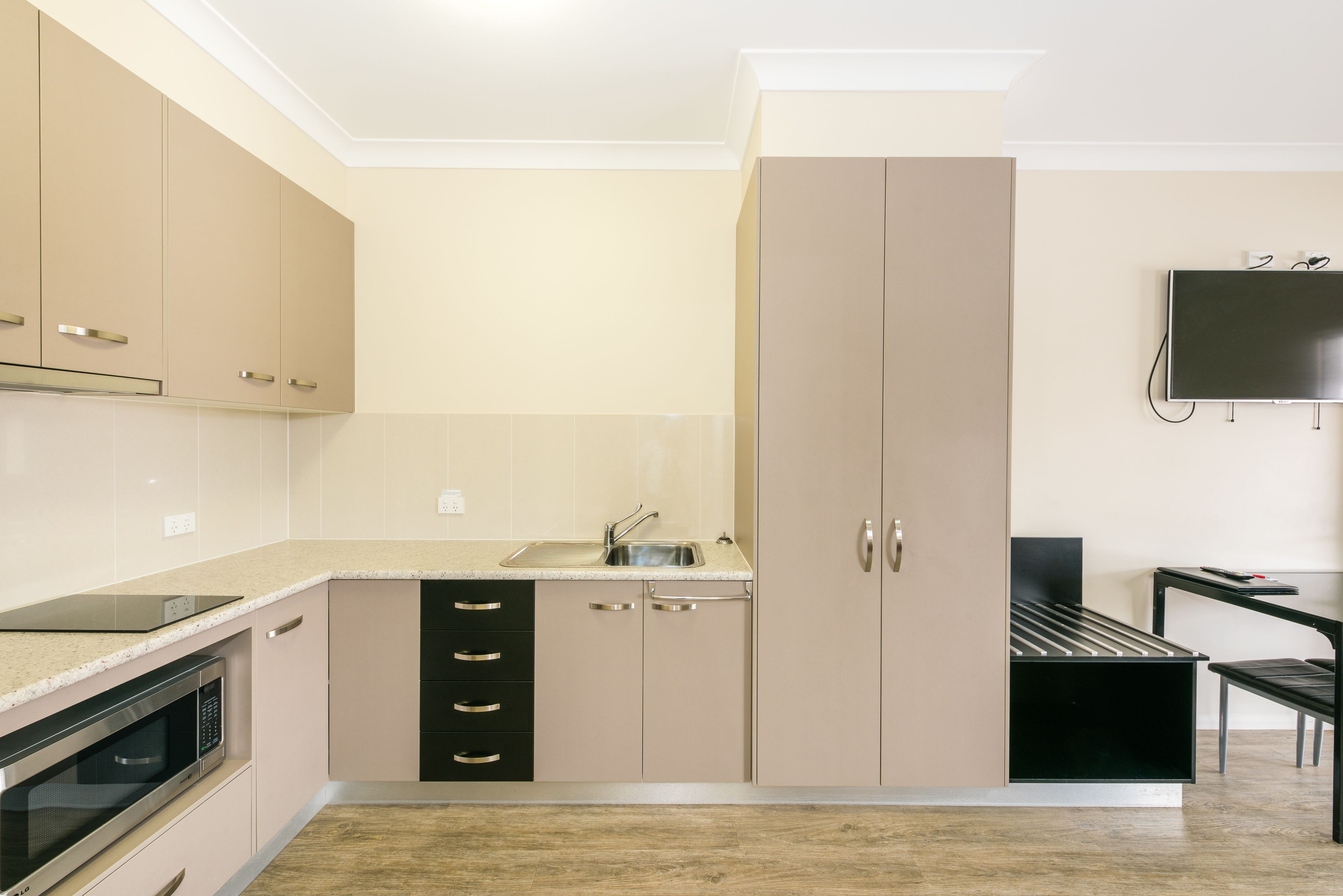 A modern kitchen with beige cabinets, a built-in microwave, and a sink.