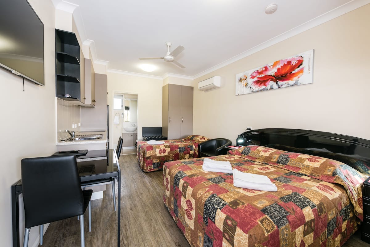 A hotel room with two beds, a desk, a chair, a ceiling fan, and a painting on the wall.