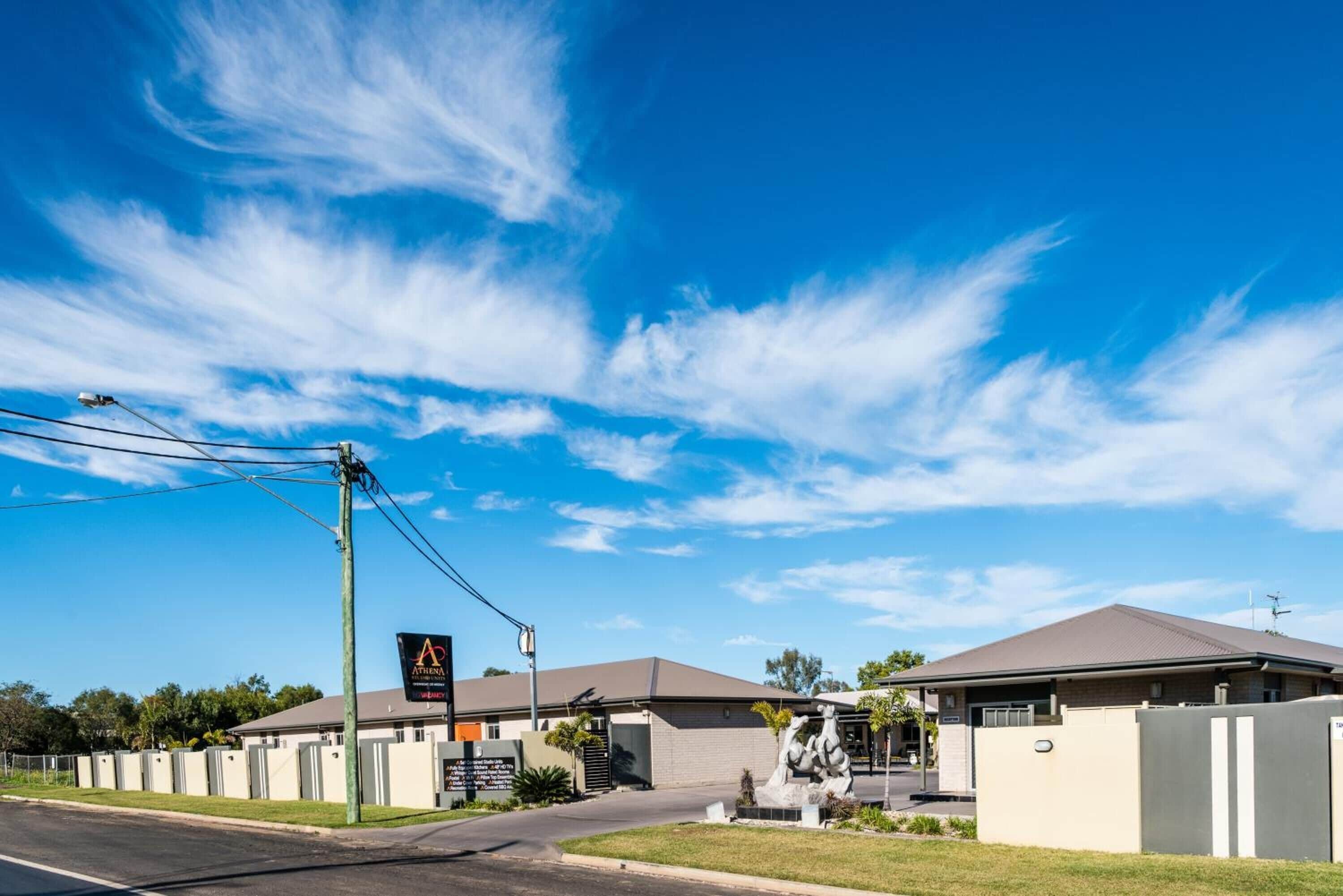 A hotel with a clear blue sky, a parking lot, and a signboard.
