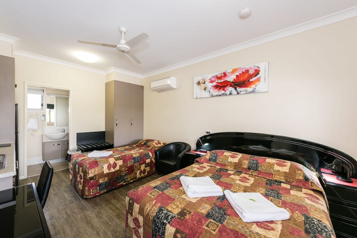A hotel room with two beds, a desk, a chair, a ceiling fan, and a bathroom visible through an open door.