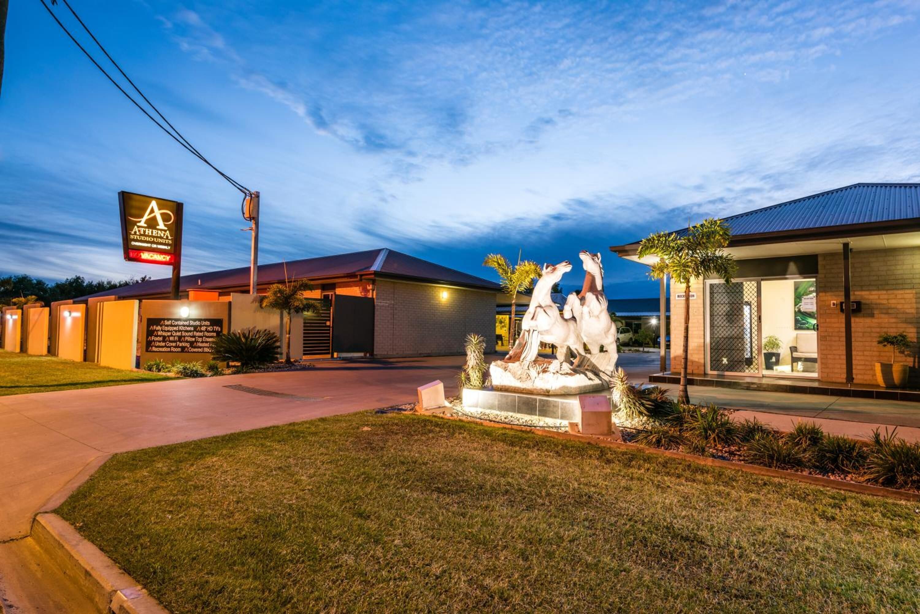 Un hotel con letrero, una estatua y un césped cuidado.