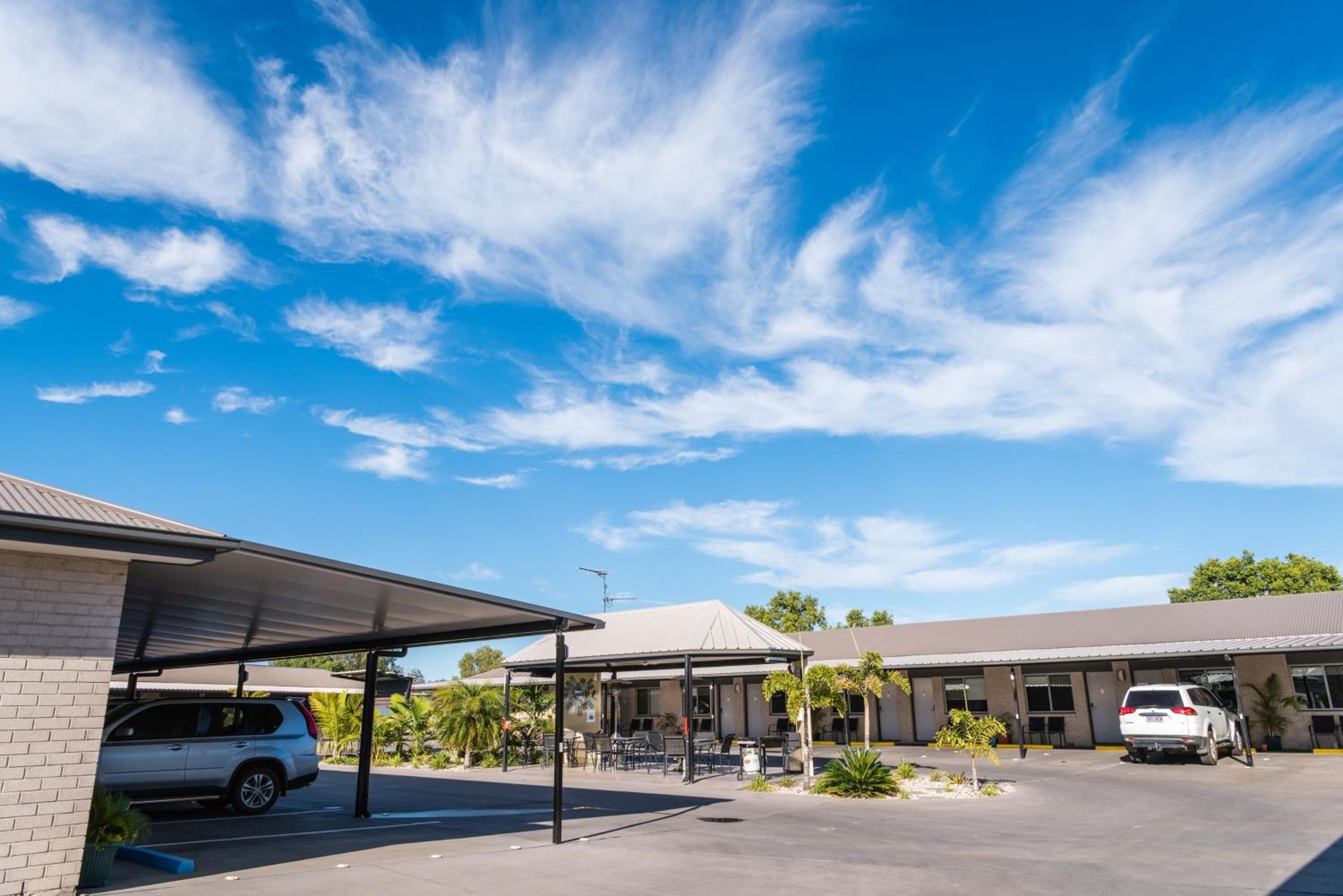 Un espace de stationnement doté d’abris pour voitures, un bâtiment à toit plat et un ciel bleu dégagé parsemé de quelques nuages.