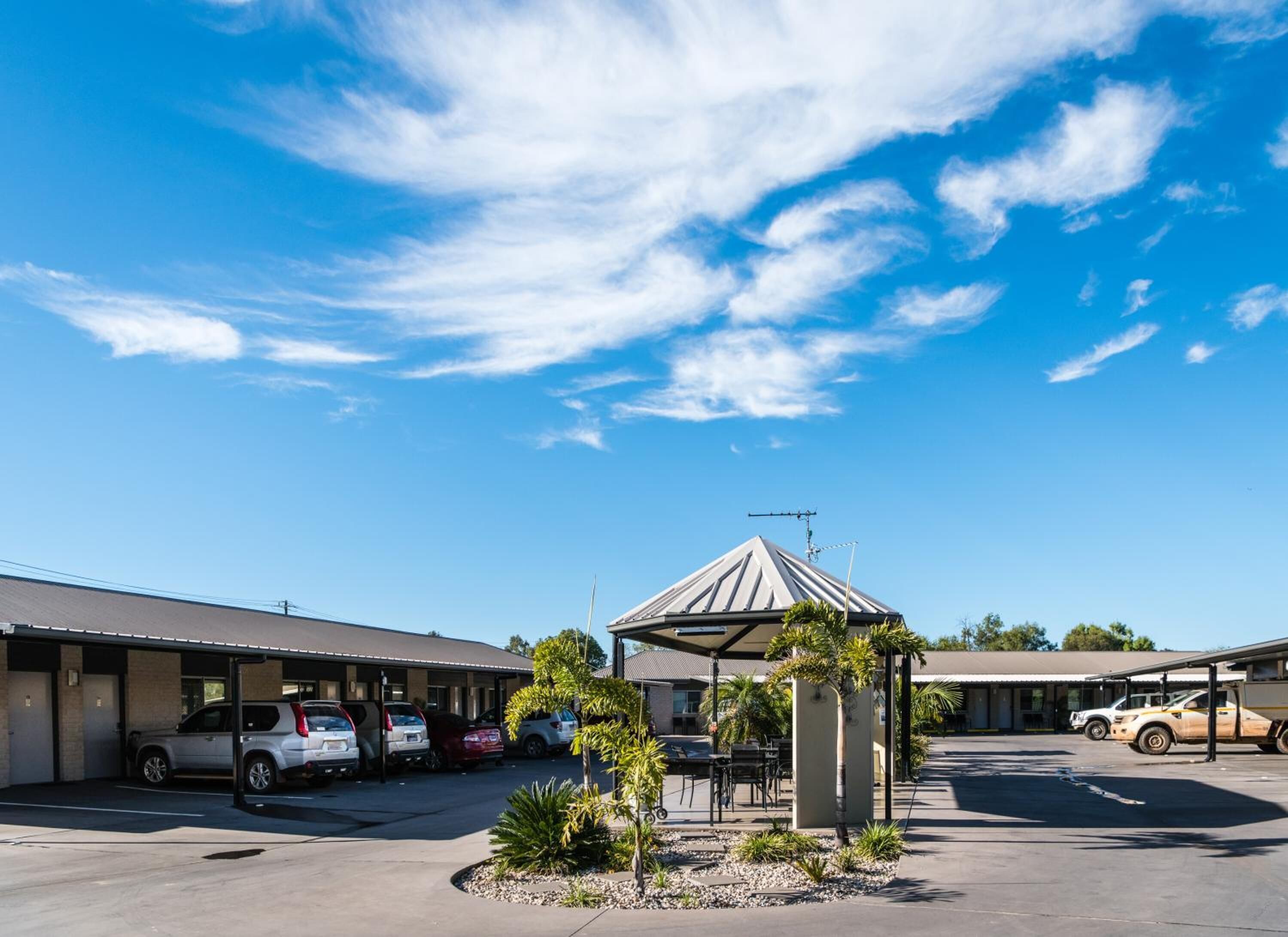 Un motel doté d’un parking, d’un espace extérieur abrité avec des sièges et d’un ciel d’un bleu éclatant.