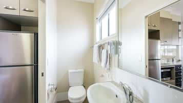 A modern bathroom with a stainless steel refrigerator, a toilet, a sink, and a large mirror.